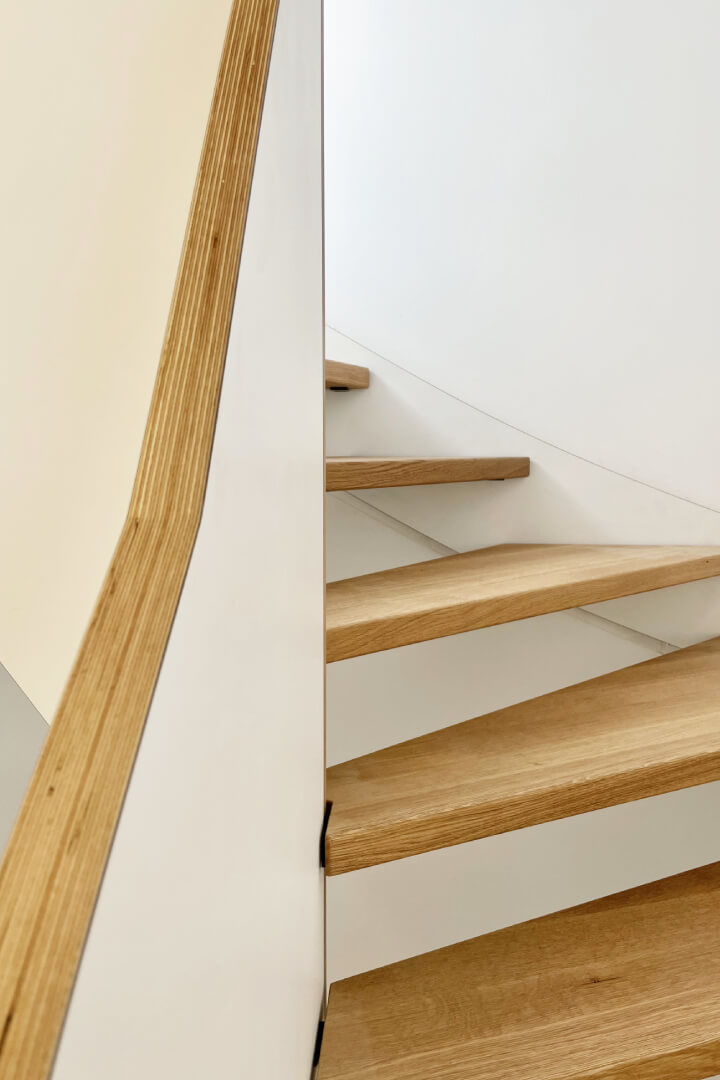 Blick auf die geländerhohe Wange der Designwangentreppe und die viertelgewendelte Lauflinie der individuell gefertigten Massivholztreppe